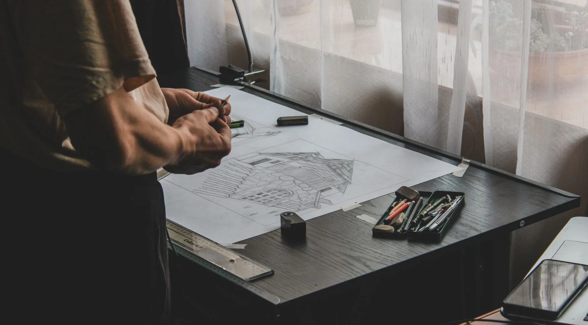 Architecte à sa table à dessin devant l’esquisse d’une maison au crayon